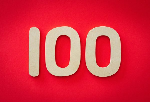 Close-up of numeral 100 in beige on a bright red background, emphasizing celebration.