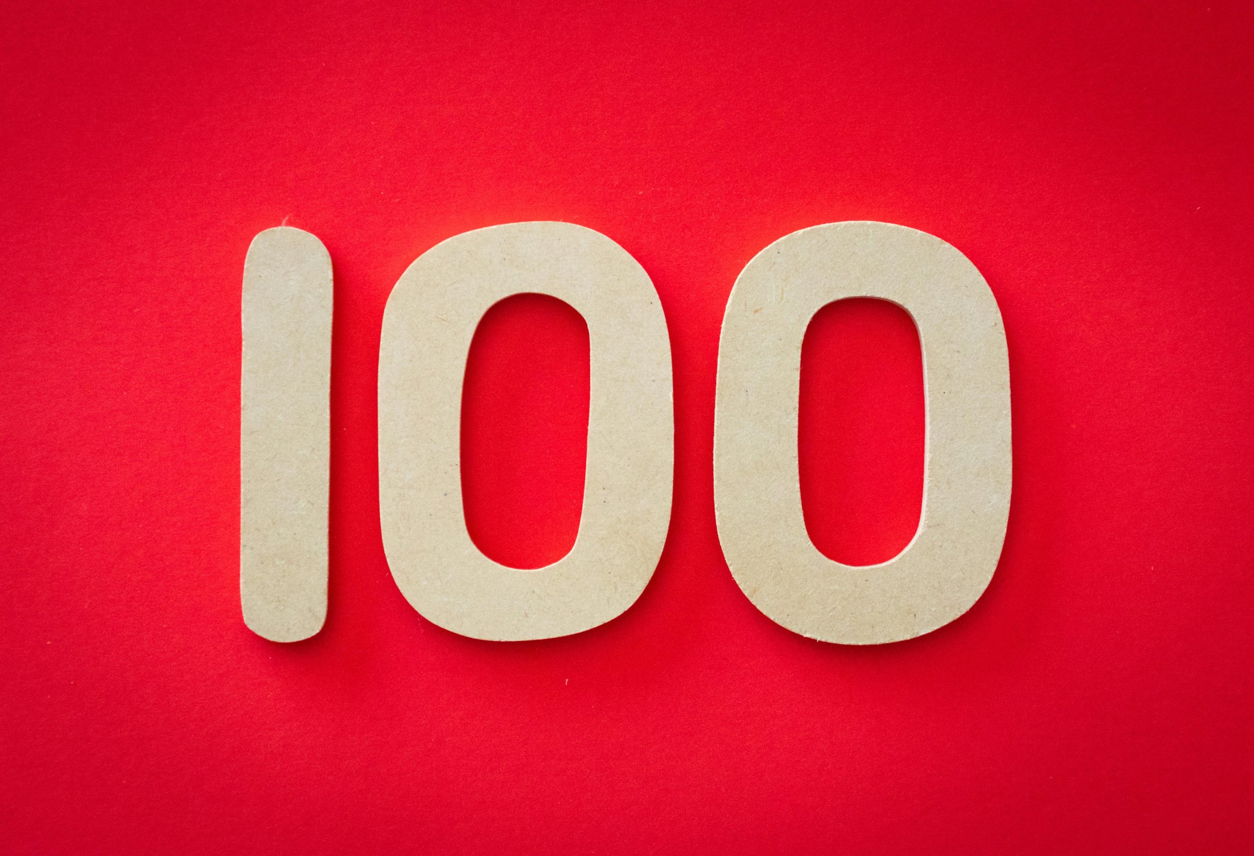 Close-up of numeral 100 in beige on a bright red background, emphasizing celebration.