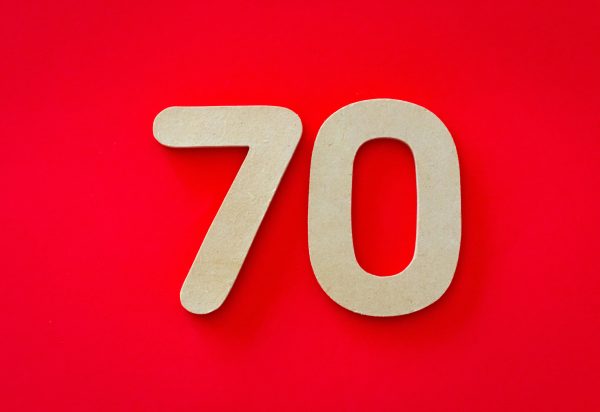 Wooden cutout of the number seventy on a vivid red background, ideal for design use.