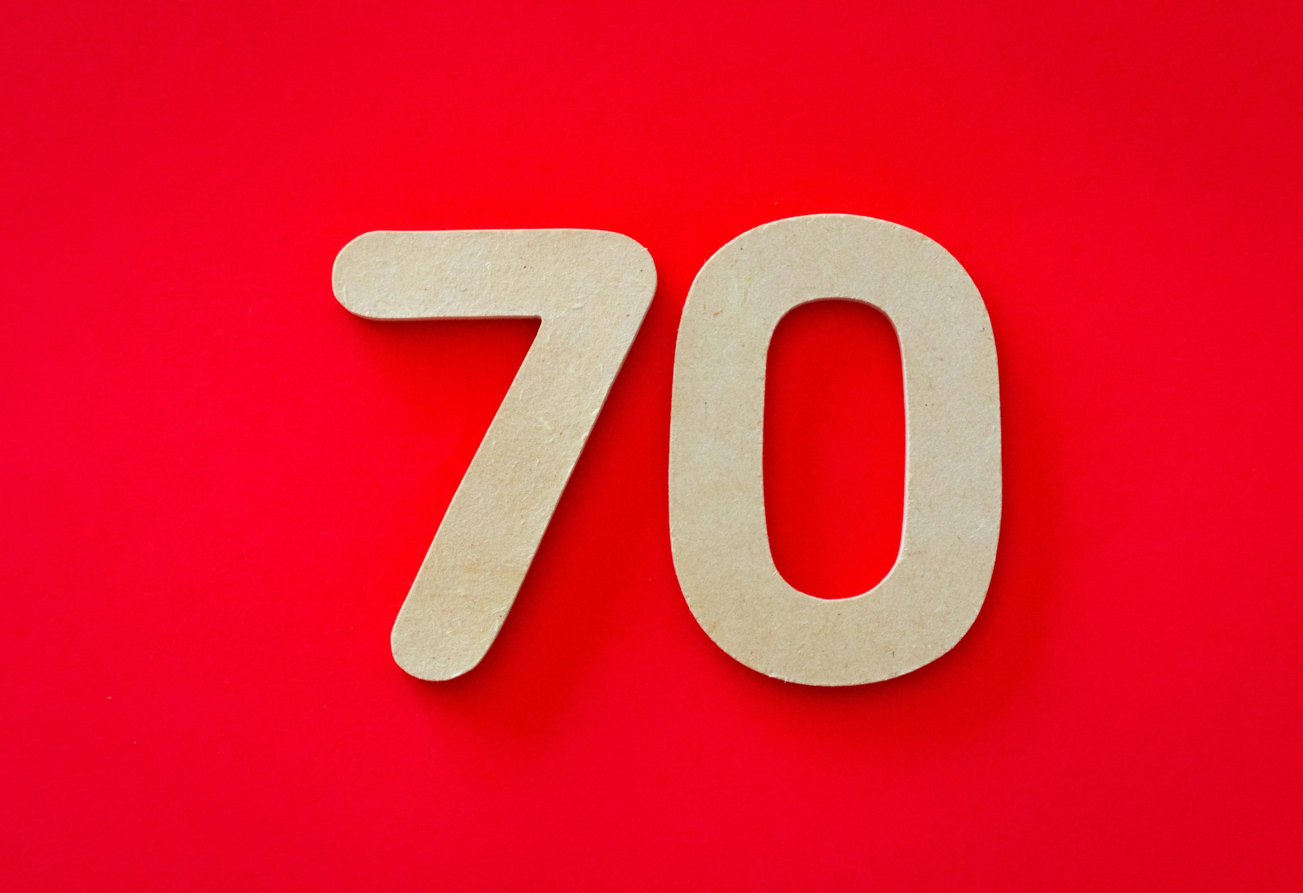 Wooden cutout of the number seventy on a vivid red background, ideal for design use.